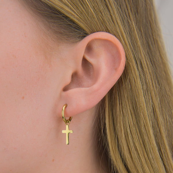 Model draagt oorbellen met een gouden kruis